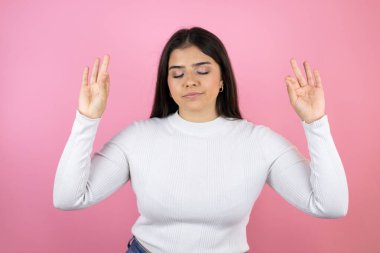 Genç, güzel bir kadın pembe arka planda. Rahat ol ve gülümse. Gözlerin kapalı meditasyon yaparken parmaklarınla hareket et.