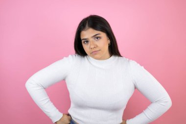 Soyutlanmış pembe arka planda genç ve güzel bir kadın. Kuşkucu ve gergin. Yüzünde tasvip etmeyen bir ifade.