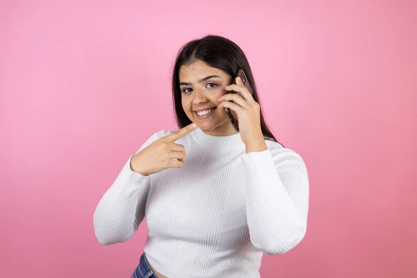 Fiatal Gyönyörű Elszigetelt Rózsaszín Háttér Mosolyog Beszél Telefonon Rámutatva Telefon — Stock Fotó