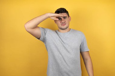 İzole edilmiş sarı arka plan üzerine gündelik tişört giyen yakışıklı genç bir adam çok mutlu ve tebessüm ediyor. arama kavramı.