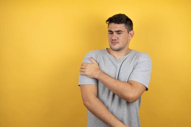 Omzunda acı ve acı dolu bir ifadeyle izole edilmiş sarı arka plan üzerine sıradan bir tişört giyen genç yakışıklı bir adam.