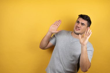 Sarı arka plan üzerine sıradan bir tişört giyen genç yakışıklı bir adam kolları yukarıdan düşmüş gibi korkmuş.