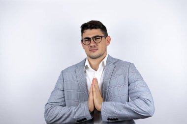 İş adamı beyaz arkaplan üzerine sıradan bir gömlek giymiş elleri ile yalvarıyor ve dua ediyor yüzünde umut ifadesi var çok duygusal ve endişeli.