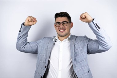 İş adamı beyaz arka planda rahat bir gömlek giyiyor. Çok mutlu ve heyecanlı. Kollarını kaldırmış, gülümseyen ve başarı için bağıran başarılı bir jest yapıyor..