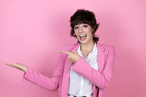 Young business woman over isolated pink background surprised, showing and pointing something that is on her hand