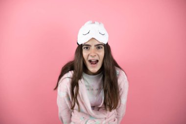 Pembe arka planda pijama ve uyku maskesi takan güzel bir kız şaşkınlık ve şaşkınlık dolu bir ifade, korku ve heyecan dolu bir yüz..