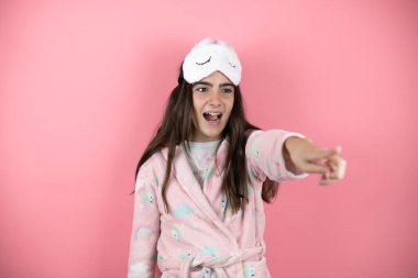 Pembe arka planda pijama ve uyku maskesi takan güzel bir kız parmağıyla işaret ederek ileriyi işaret ediyor, ağzı açık hayret verici bir ifade, önde bir şey.