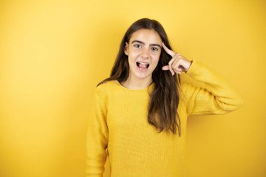 Pretty girl wearing a yellow sweater standing over isolated yellow background smiling and thinking with her fingers on her head that she has an idea.