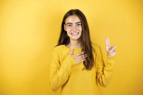 Pretty girl wearing a yellow sweater standing over isolated yellow background smiling swearing with hand on chest and fingers up, making a loyalty promise oath