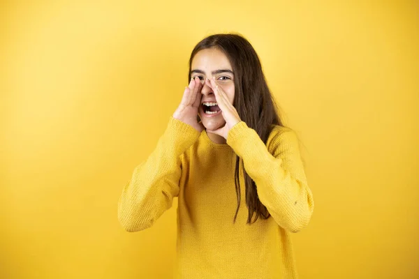 可愛いです女の子身に着けていますA黄色セータースタンディング上の隔離された黄色の背景叫びと叫び大声で側に手で口 — ストック写真