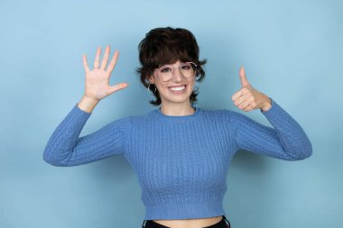 Young caucasian woman over isolated blue background showing and pointing up with fingers number six while smiling confident and happy