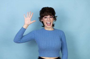 Young caucasian woman over isolated blue background showing and pointing up with fingers number five while smiling confident and happy