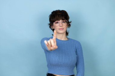 Young caucasian woman over isolated blue background showing and pointing up with fingers number one while is serious