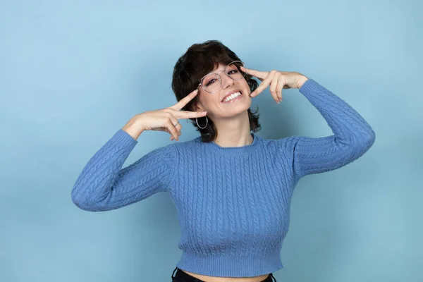 stock image Young caucasian woman over isolated blue background Doing peace symbol with fingers over face, smiling cheerful showing victory