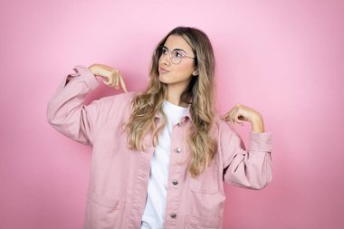 Pembe arka planda duran uzun saçlı güzel sarışın kadın tişörtünü tutarken başarılı bir ifade takınıyor.