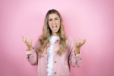 Pembe arka planda duran uzun saçlı genç, güzel sarışın kadın. Deli gibi bağırıyor ve agresif bir ifade ve kollarla bağırıyor. Hayal kırıklığı konsepti.