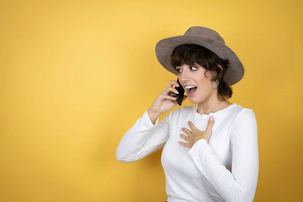 Sarı Arka Planda Şapka Takan Beyaz Bir Kadın Telefonda Endişeli — Stok fotoğraf