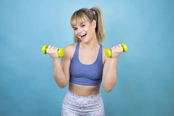 Young beautiful woman wearing sportswear holding a bottle of water over isolated blue background holding a dumbbells