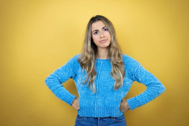 Sarı arka planda duran uzun saçlı güzel sarışın kadın şüpheci ve gergin, yüzünde onaylamayan ifade.