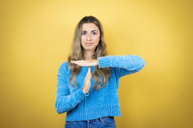 Sarışın, uzun saçlı, sarı arka planda duran güzel bir kadın. Elleriyle hareket ediyor, hayal kırıklığına uğramış ve ciddi bir yüz ifadesi var.
