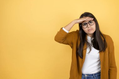 İzole edilmiş sarı arka planda ceket giyen genç ve güzel bir kadın çok mutlu ve tebessüm ediyor. arama kavramı.