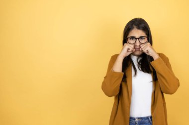 İzole edilmiş sarı arka planda ceket giyen genç ve güzel bir kadın depresif ve endişeli, sinirli ve korkmuş bir şekilde ağlıyor. Üzücü ifade.