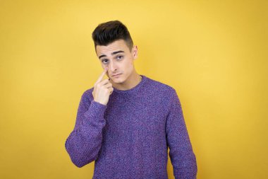 İzole edilmiş sarı arka planda genç beyaz bir adam. Gözünü dikip jestini izliyor. Şüpheli bir ifade.