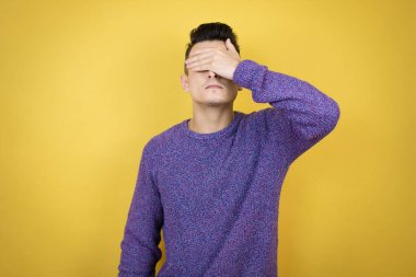 Kafkasyalı genç, izole edilmiş sarı arka plan ciddi ve eliyle gözlerini kapatıyor.