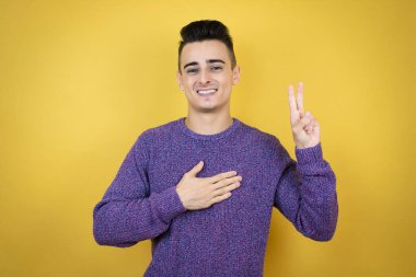 İzole edilmiş sarı arka planda genç beyaz bir adam gülümsüyor. Göğsü ve parmakları havada küfür ediyor. Sadakat yemini ediyor.