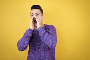 İzole edilmiş sarı arka planda genç beyaz bir adam elleri ağızda bağırıyor ve bağırıyordu.