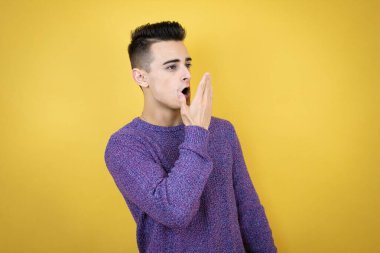 Kafkas asıllı genç bir adam, sarı arka planda, eli ağzında ve şaşırmış, yan bakıyor.