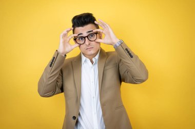 İzole edilmiş sarı arka planda genç bir iş adamı parmaklarıyla gözlerini açmaya çalışıyor, uykulu ve yorgun bir şekilde sabah yorgunluğu çekiyor.