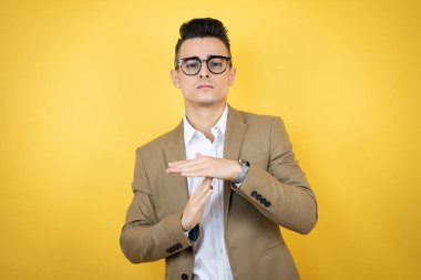 Soyutlanmış sarı arka planda genç bir iş adamı. Elleriyle jest yapıyor, hayal kırıklığına uğramış ve ciddi bir yüz ifadesi takınıyor.