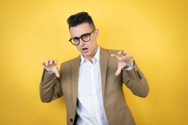 Genç iş adamı izole edilmiş sarı arka planda gülümsüyor. Pençe hareketlerini kedi gibi yapıyor. Agresif ve seksi bir ifade.