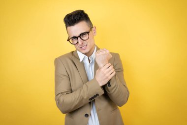 İzole edilmiş sarı arka planda yaşayan genç bir iş adamı. Ellerinde ve parmaklarında ağrı, eklem iltihabı.