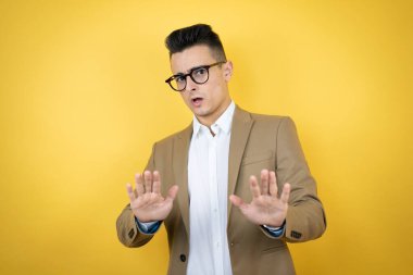 Soyutlanmış sarı arka planda genç bir iş adamı. Korkudan ve korkudan dehşete düşmüş. El hareketlerini durdur, şok içinde bağır. Panik konsepti.