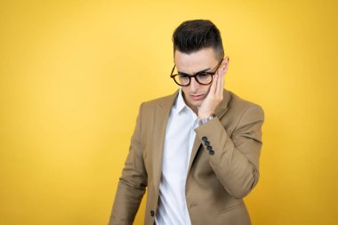 İzole edilmiş sarı arka plan üzerinde genç bir iş adamı diş ağrısı ya da diş hastalığından dolayı acı dolu bir ifadeyle ağıza dokunuyor.