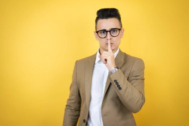 Soyutlanmış sarı arka planda genç bir iş adamı parmakları dudaklarında sessiz olmak istiyor. Sessizlik ve gizli konsept.