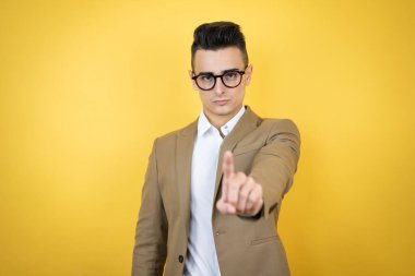 İzole edilmiş sarı arka planda genç bir iş adamı bir numarayı işaret ederken ciddi.
