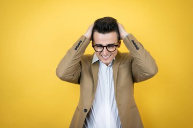 Genç iş adamı sarı arka planda çaresiz ve stresli baş ağrısından muzdarip çünkü elleri başının üstünde acı ve migren.