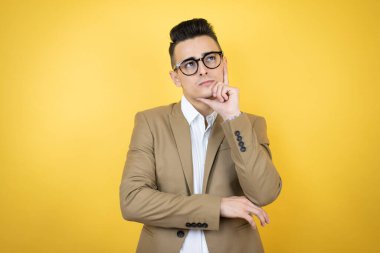 Soyutlanmış sarı arka planda genç bir iş adamı. Düşünüp yan tarafa bakıyor.