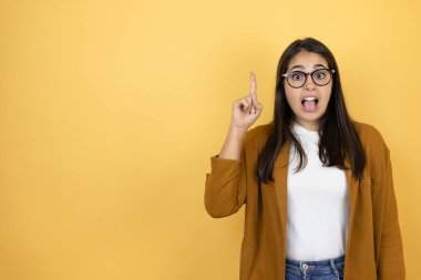İzole edilmiş sarı arka plan üzerine ceket giyen genç ve güzel bir kadın parmağını kafasında gezdirerek bir fikri olduğunu düşünmesine şaşırdı..