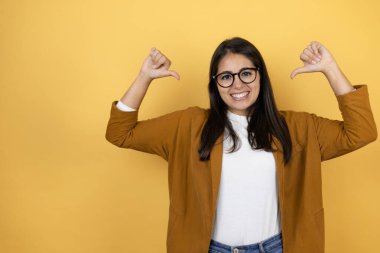 İzole edilmiş sarı arka planda ceket giyen genç ve güzel bir kadın. Kendine güvenen, yüzünde gülümseme olan, kendini gururlu ve mutlu gösteren bir kadın..
