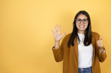 İzole edilmiş sarı arka planda ceket giyen genç ve güzel bir kadın altı numaralı parmaklarıyla gülümseyerek kendinden emin ve mutlu bir şekilde onu işaret ediyor.