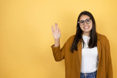 İzole edilmiş sarı arka planda spor ceket giyen güzel bir kadın Star Trek ucube sembolü yapıyor.