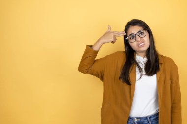 İzole edilmiş sarı arka planda ceketini giyen genç ve güzel bir kadın kendini silahla ve parmaklarıyla vurarak öldürüyor. İntihar jesti..