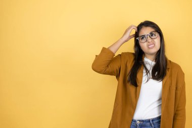 İzole edilmiş sarı arka planda ceket giyen genç ve güzel bir kadın soru sormayı merak ediyor. Şüpheyle karışık, kafa kafaya düşünerek.