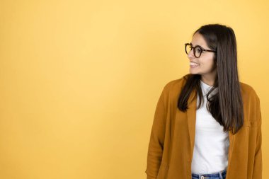 İzole edilmiş sarı arka planda ceket giyen güzel bir kadın yan tarafa gülümsüyor.