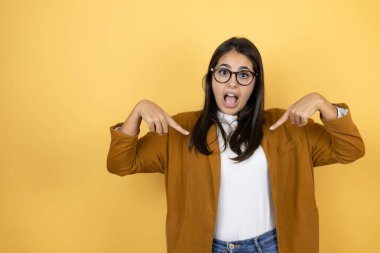 İzole edilmiş sarı arka planda ceket giyen genç ve güzel bir kadın. Kendine güvenen, yüzünde gülümseme olan, kendini gururlu ve mutlu gösteren bir kadın..