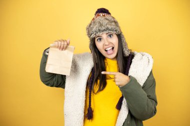 Sarı arka plan üzerinde yeşil kışlık ceket ve şapka giyen genç bir kadın. Şapka takan güzel bir kadın. Sarı arka plan üzerinde yeşil bir kışlık ceket.